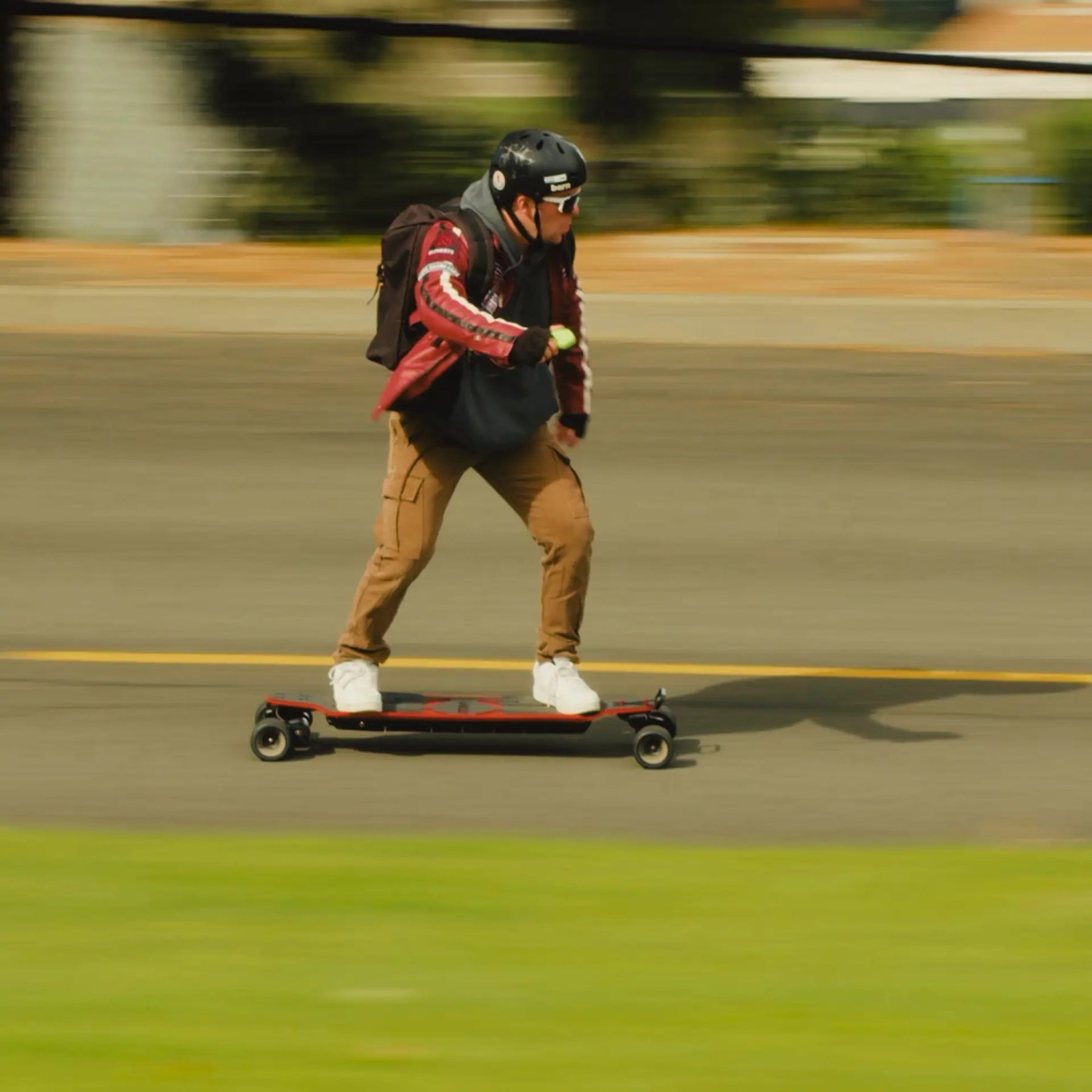 A man riding on OMW Lancer electric skateboard with a red deck on a road