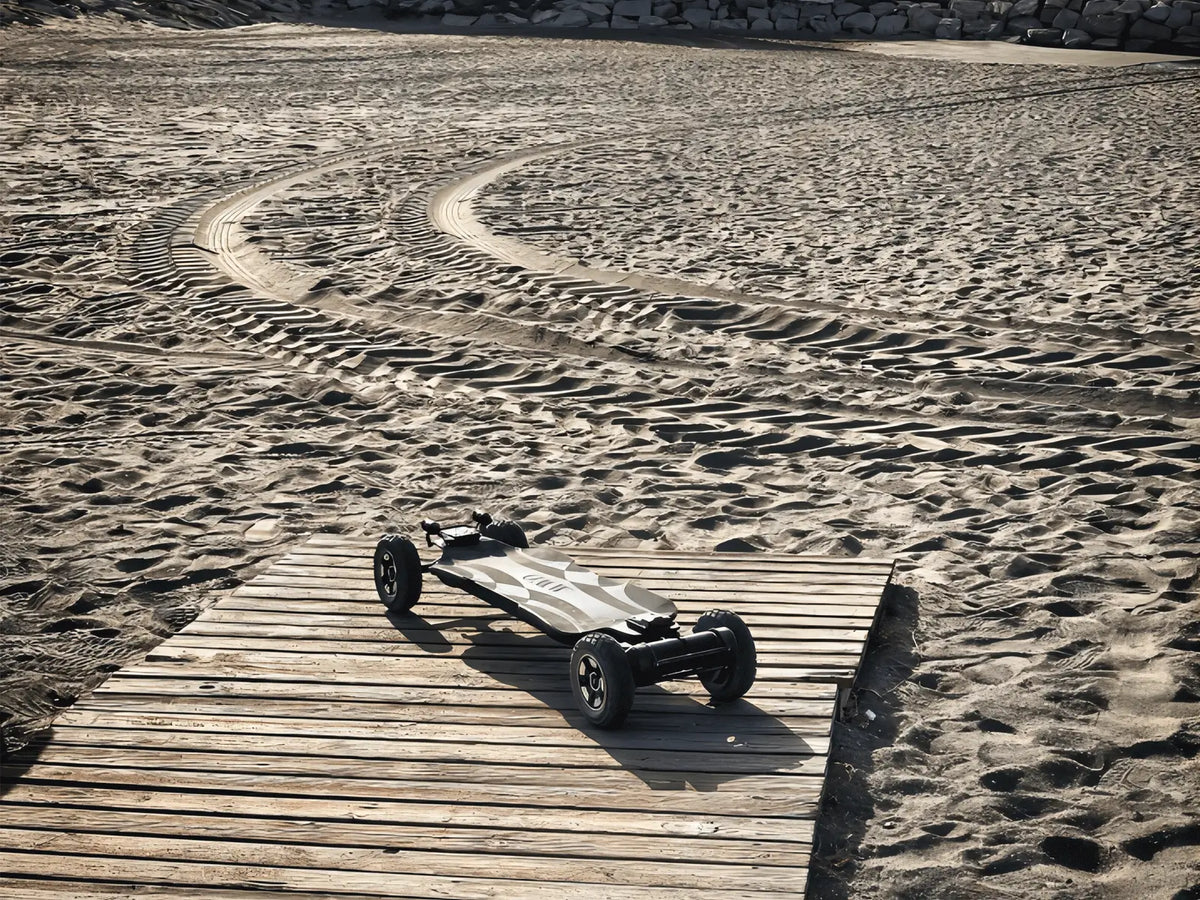 OMW Cavalry all-terrain electric skateboard beside tire tracks on sand