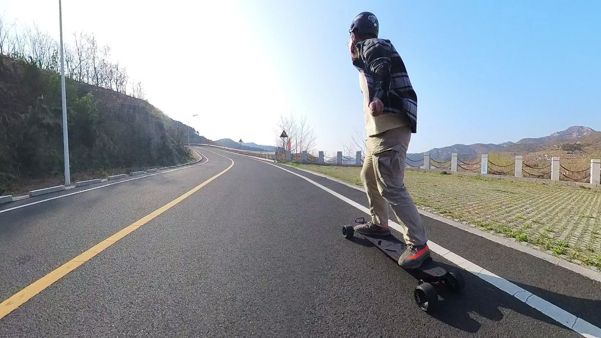 Helmeted rider climbing a dry paved hill on an OMW Lancer electric skateboard with 125 mm wheels